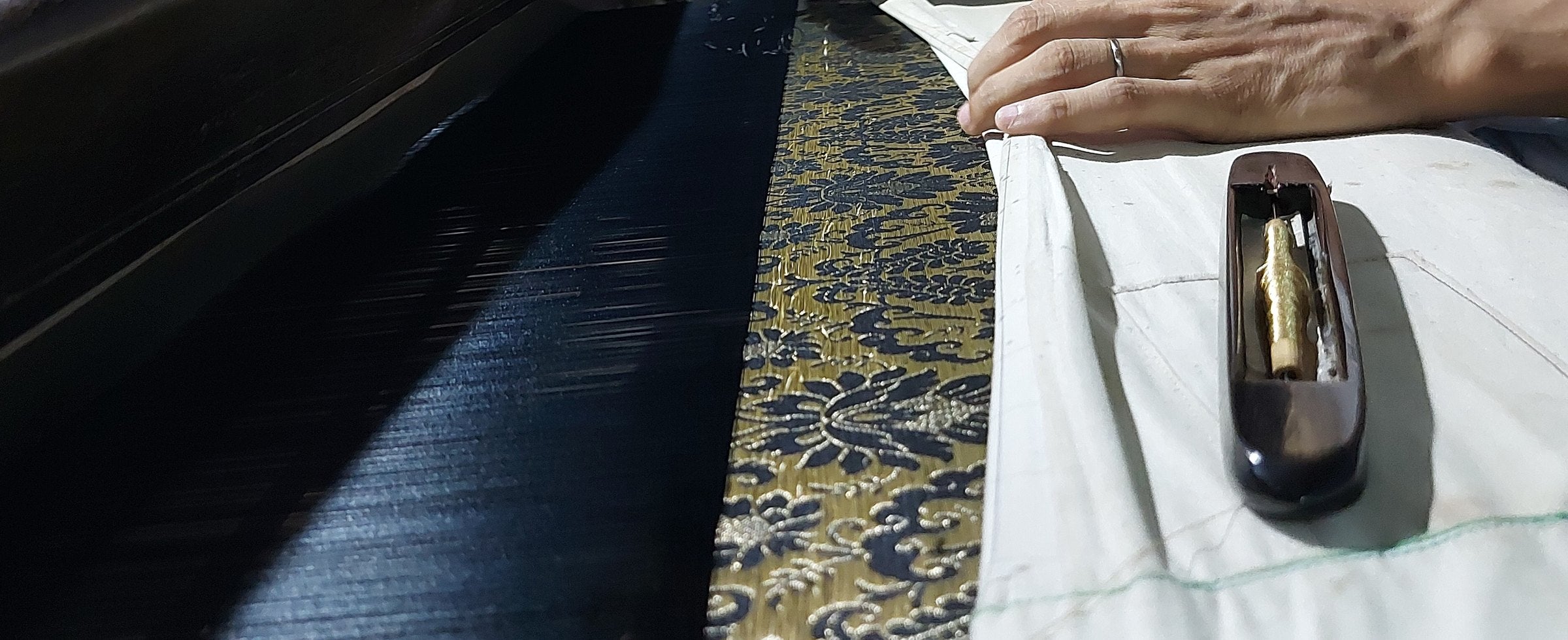 A weaver at a handloom, seen through the warp threads